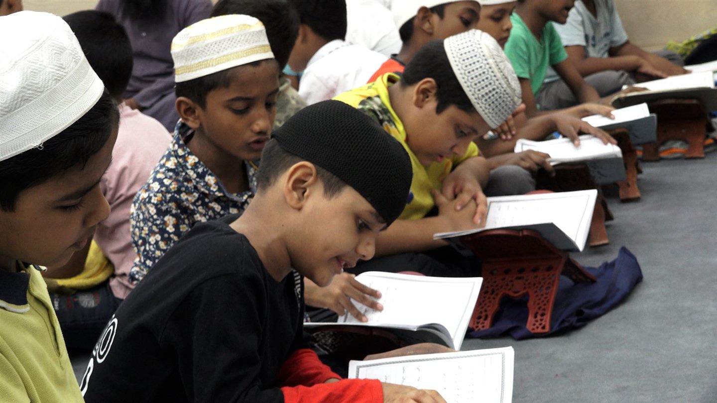 Children sitting together with open books on wooden stands in a classroom.